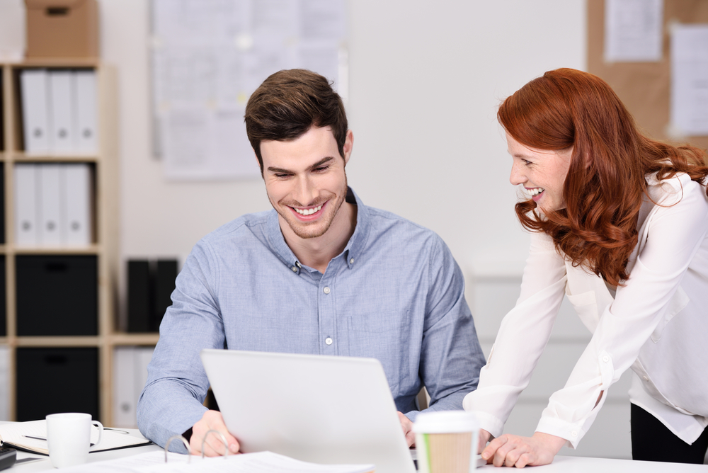 Happy Young Business Couple Watching Something at Laptop Computer on Top of the Office Table.